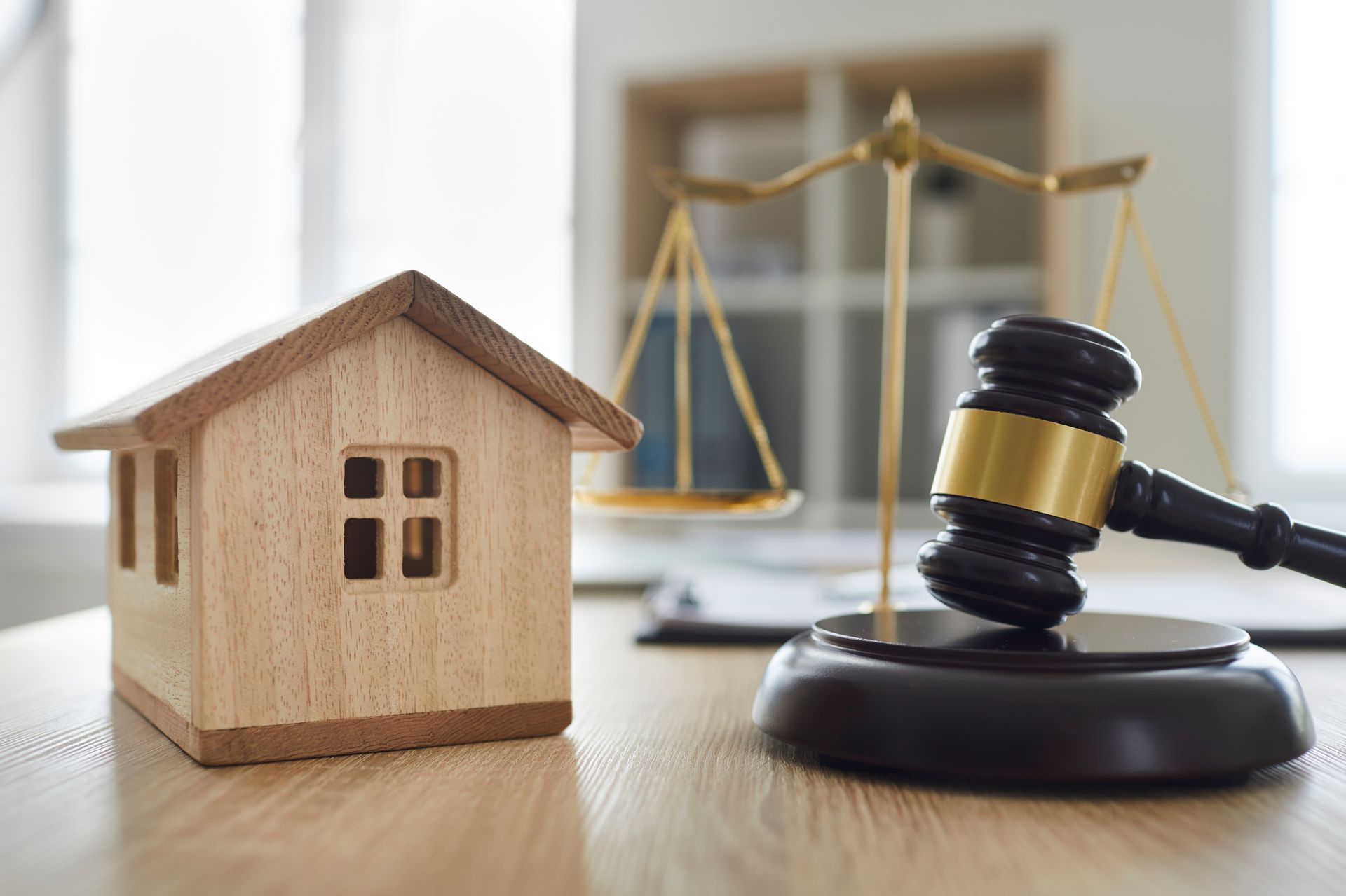Wooden house model beside a gavel and scales of justice, symbolizing property law or real estate disputes