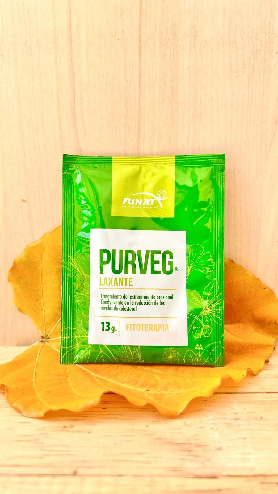 Envase verde de PURVEG sobre una superficie de madera con hojas naranjas debajo.