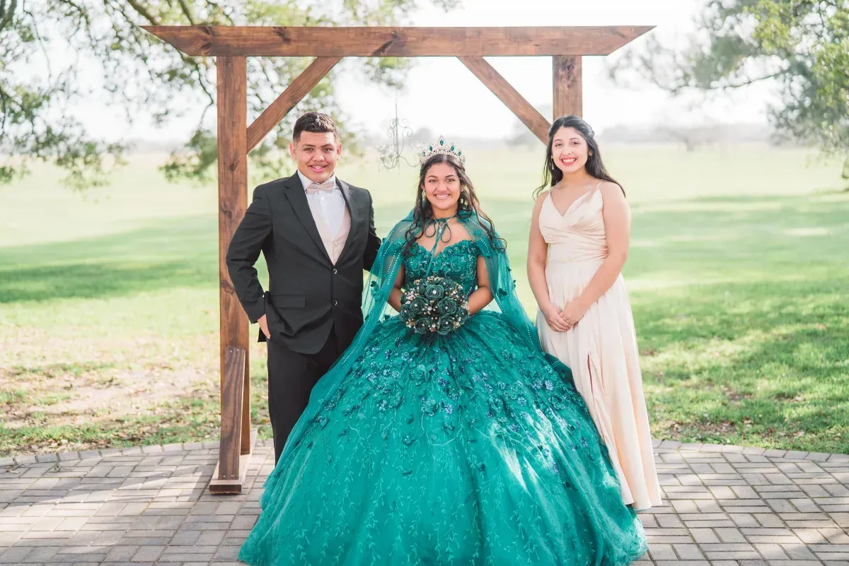 A woman in a green dress is standing next to a man and a woman in a white dress.