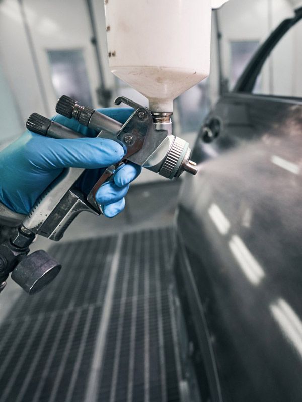 Autobody paint technician spray painting a car door.