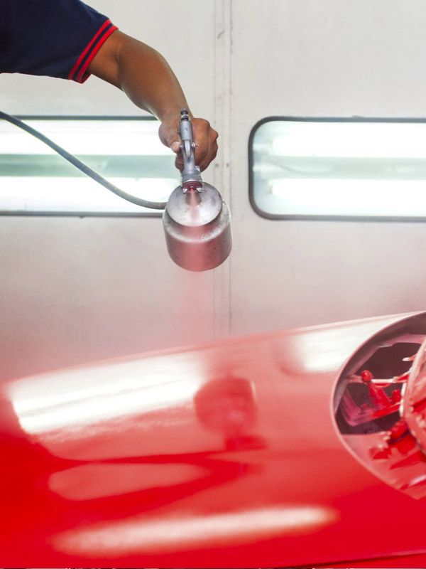 Paint tech spraying red paint on a car hood. Paint tech spraying red paint on a car hood