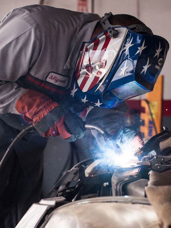 Welder repairing a car after a front end collision.