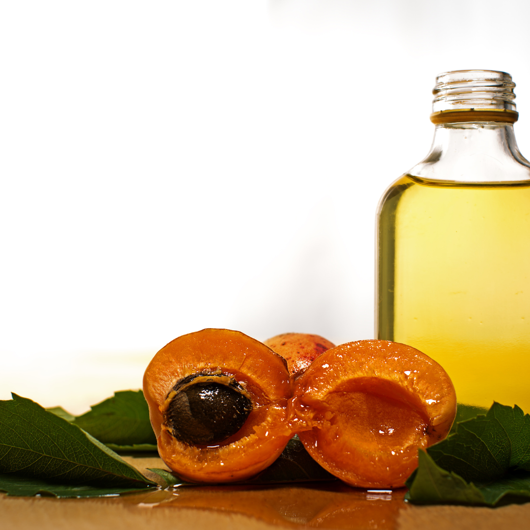 A bottle of oil next to a sliced apricot on a table.