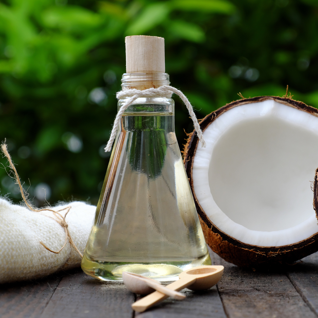 A bottle of coconut oil next to a coconut and two wooden spoons