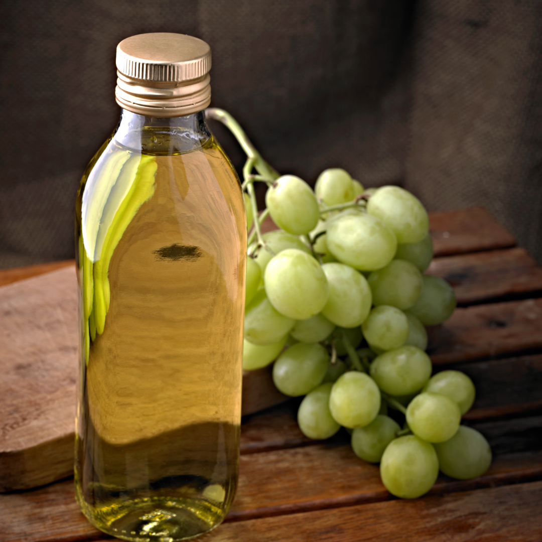 A bottle of olive oil next to a bunch of green grapes