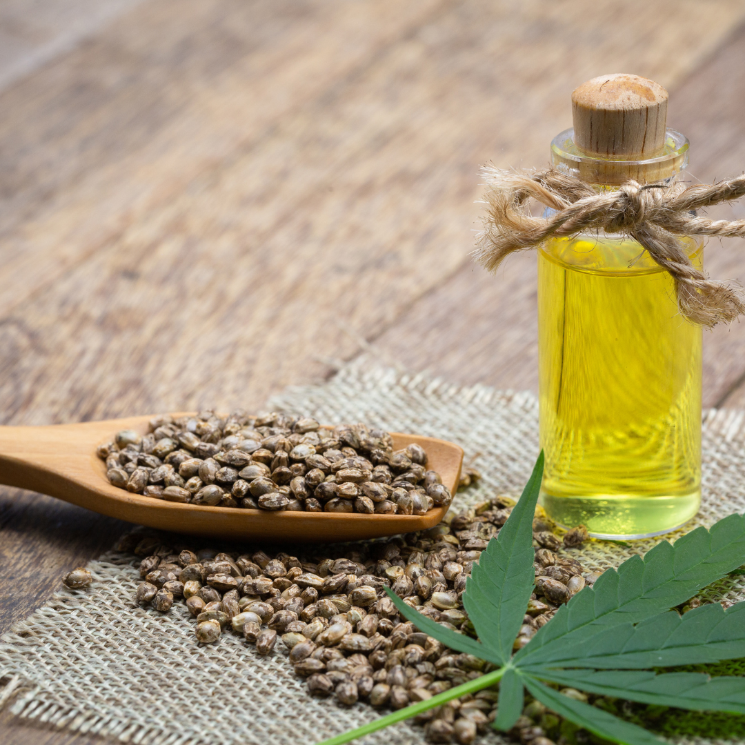 A wooden spoon filled with hemp seeds next to a bottle of oil.