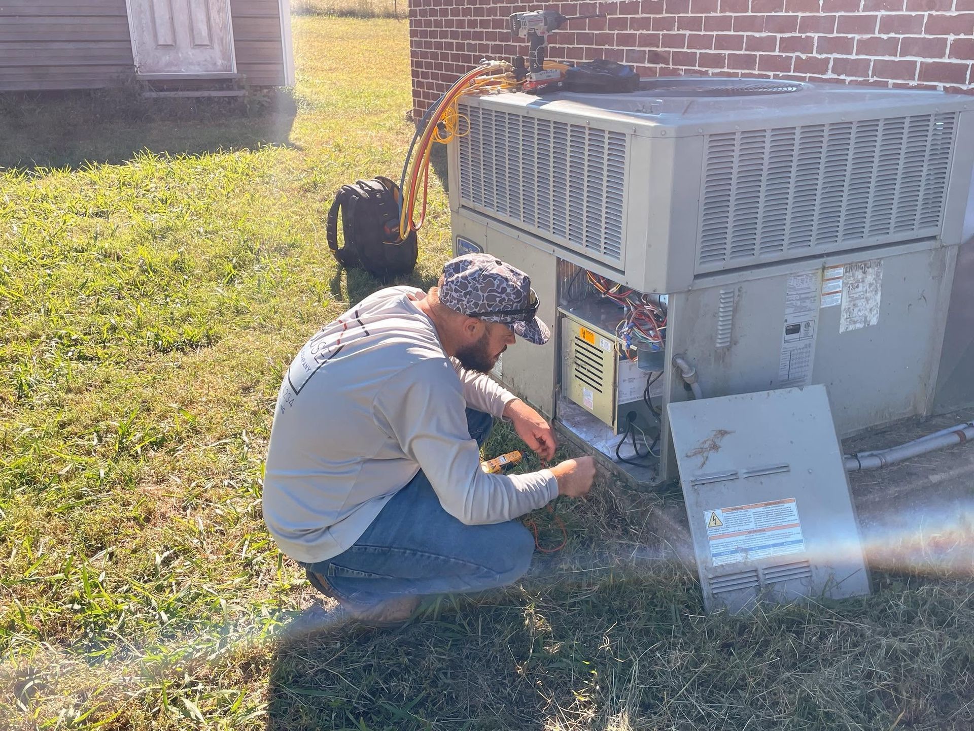 An air conditioner is sitting on the ground in front of a white brick building.