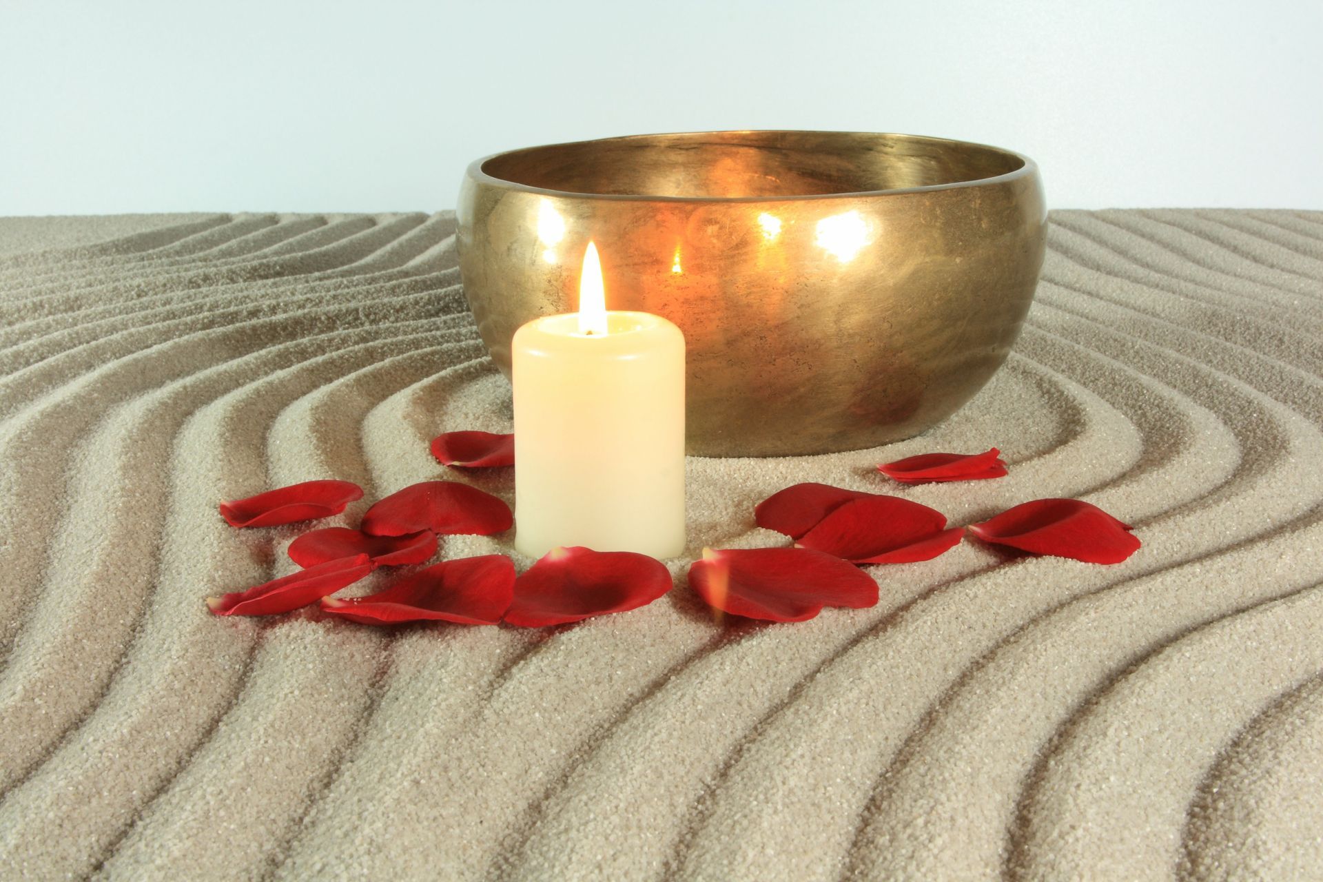 Meditationsschale, brennende Kerze und rote Blütenblätter in einem Zen-Sandgarten