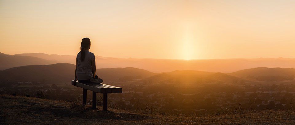 Eine Frau meditiert in eine ruhigen Berglandschaft - Was ist Achtsamkeit