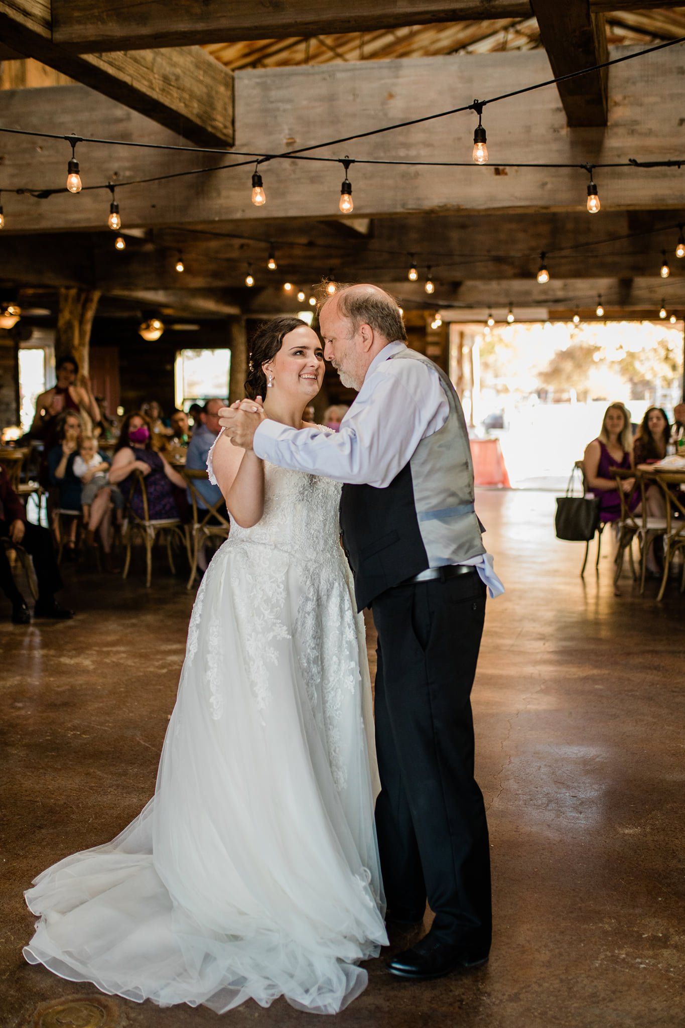 A bride and groom share their first dance at their wedding, with the bride wearing a white lace gown