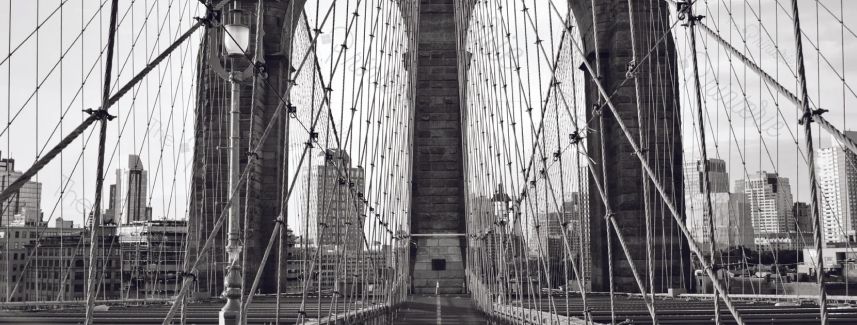Black-and-white view of the Brooklyn Bridge pedestrian walkway with Manhattan skyline beyond