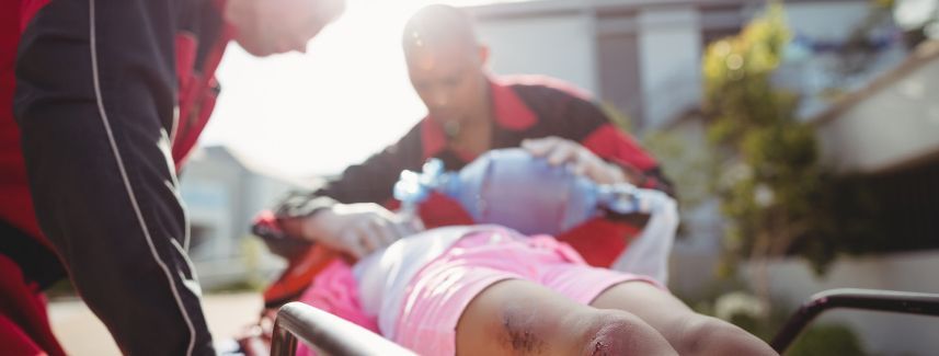 Paramedics wheeling an injured person on a stretcher outdoors in bright sunlight