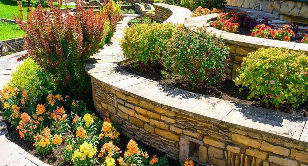 A stone wall surrounded by flowers and bushes in a garden.