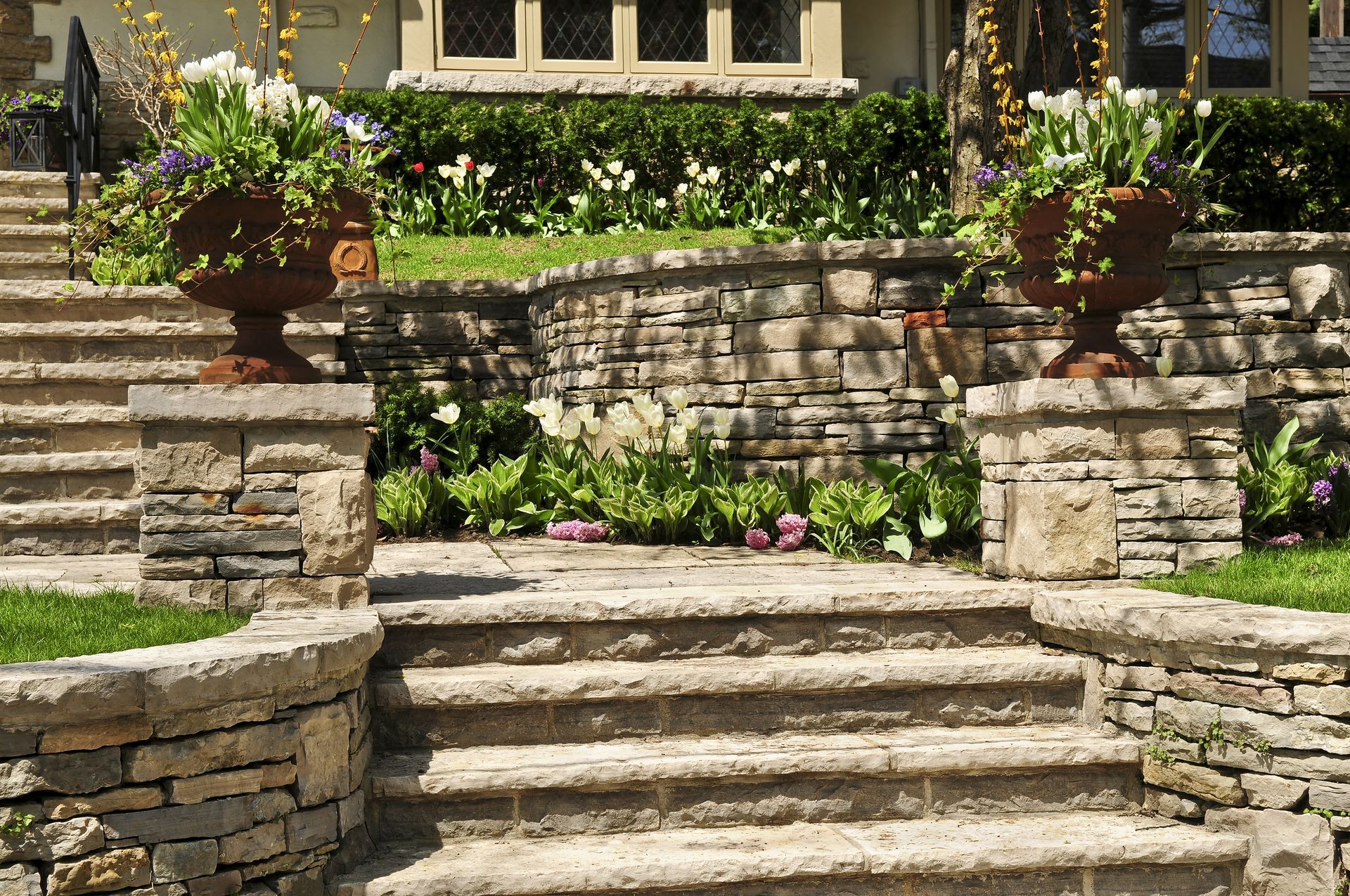 A stone wall surrounds a set of stairs leading up to a house.