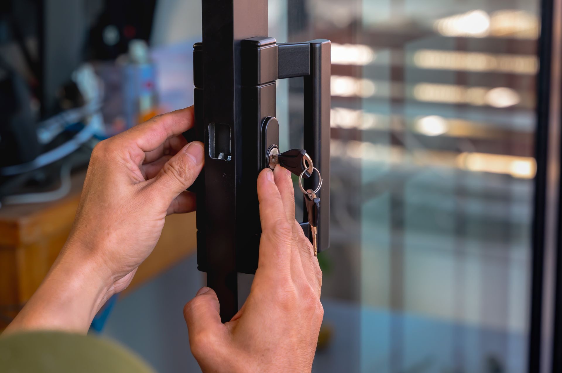 Hands securing a black door lock on a glass door with a key fob.