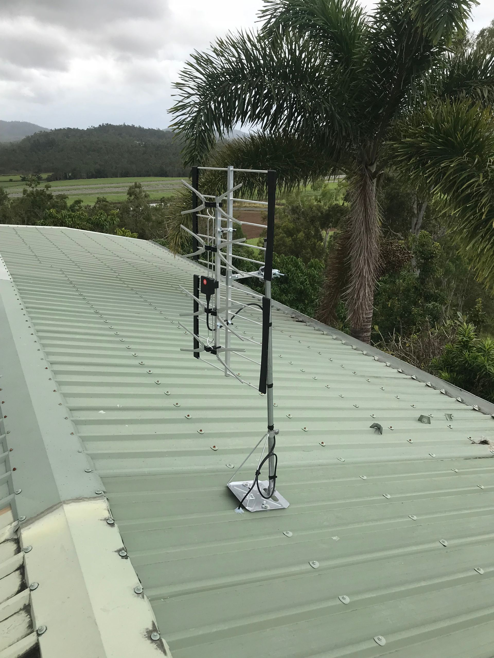 Television antenna mounted on a green metal roof with a view of hills and trees.