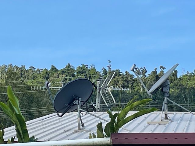 Satellite dishes on a rooftop with a forest and blue sky background.