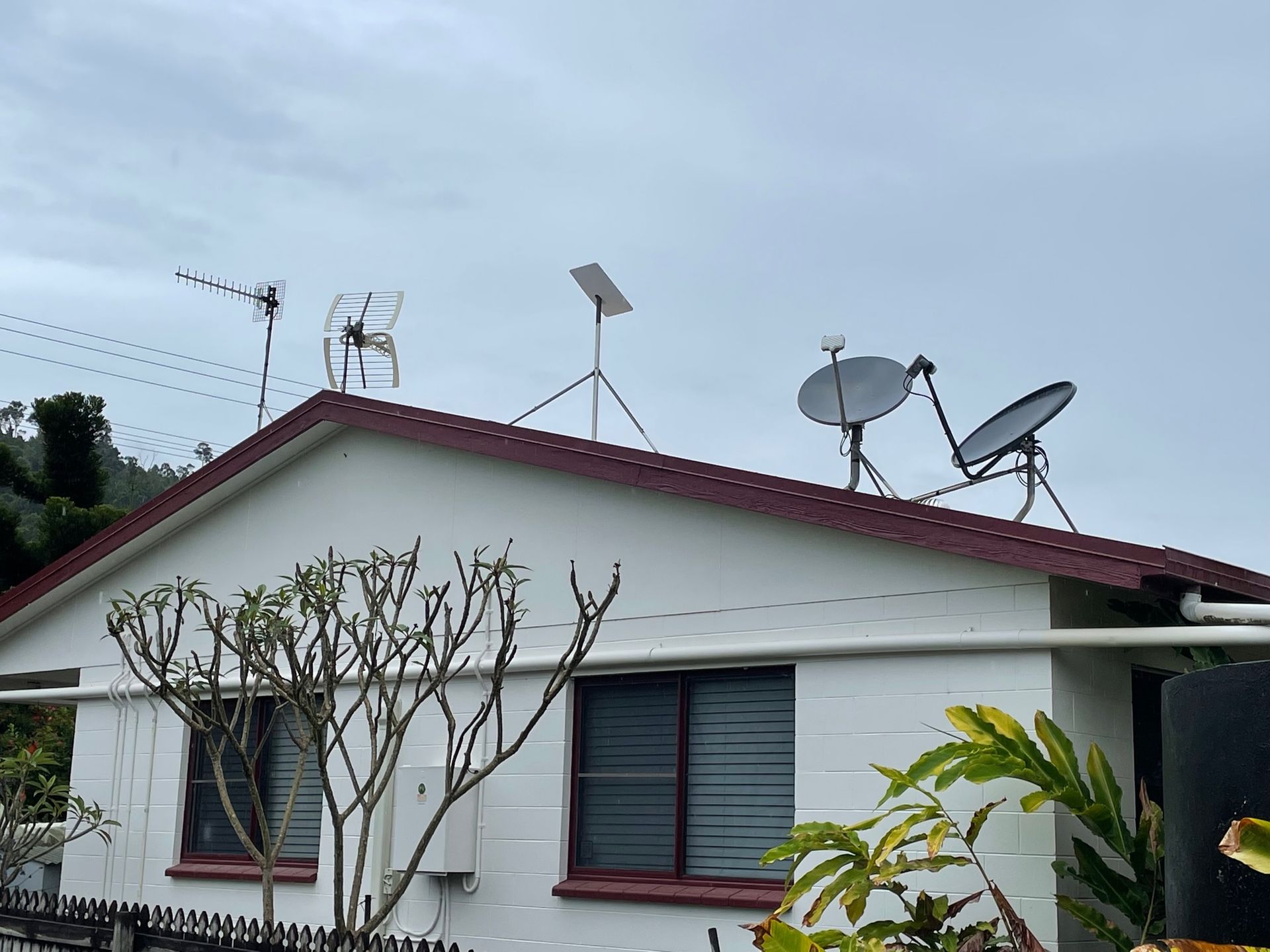 White house roof with several antennas and satellite dishes. Overcast sky.
