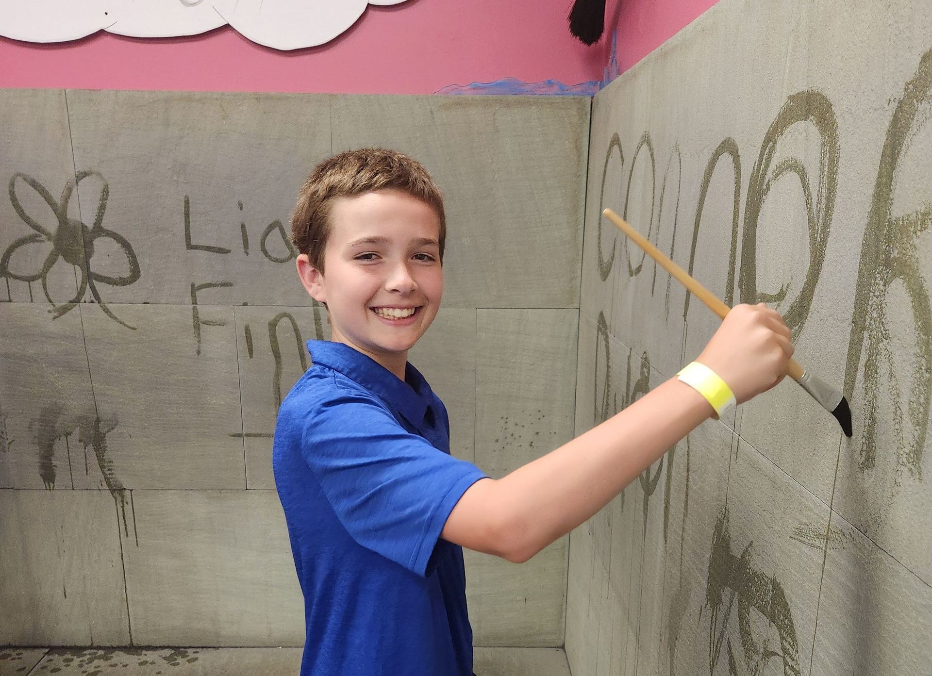 A boy in a blue shirt is drawing on a wall with a brush