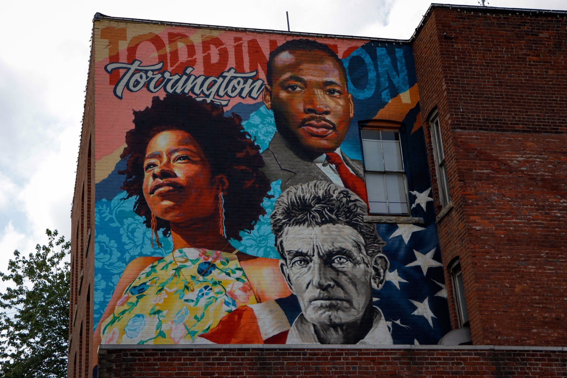 A large mural on the side of a brick building shows a woman a man and an american flag
