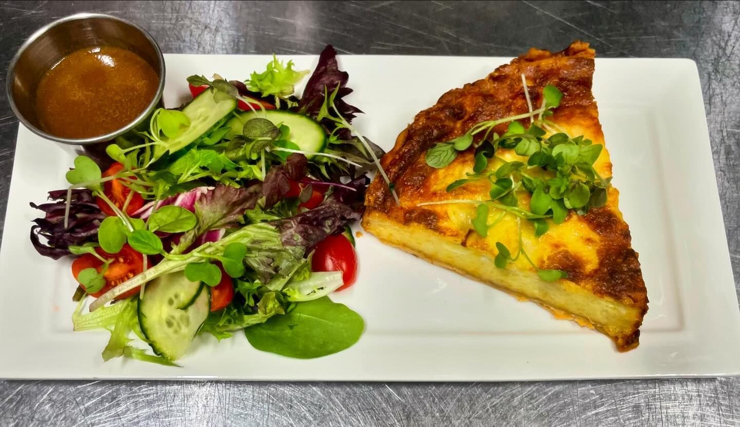 A white plate topped with a slice of quiche and a salad.