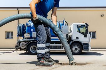 Un camion MAN bianco all'interno di un garage, con un container grigio scuro, parcheggiato davanti a una grande porta rossa.