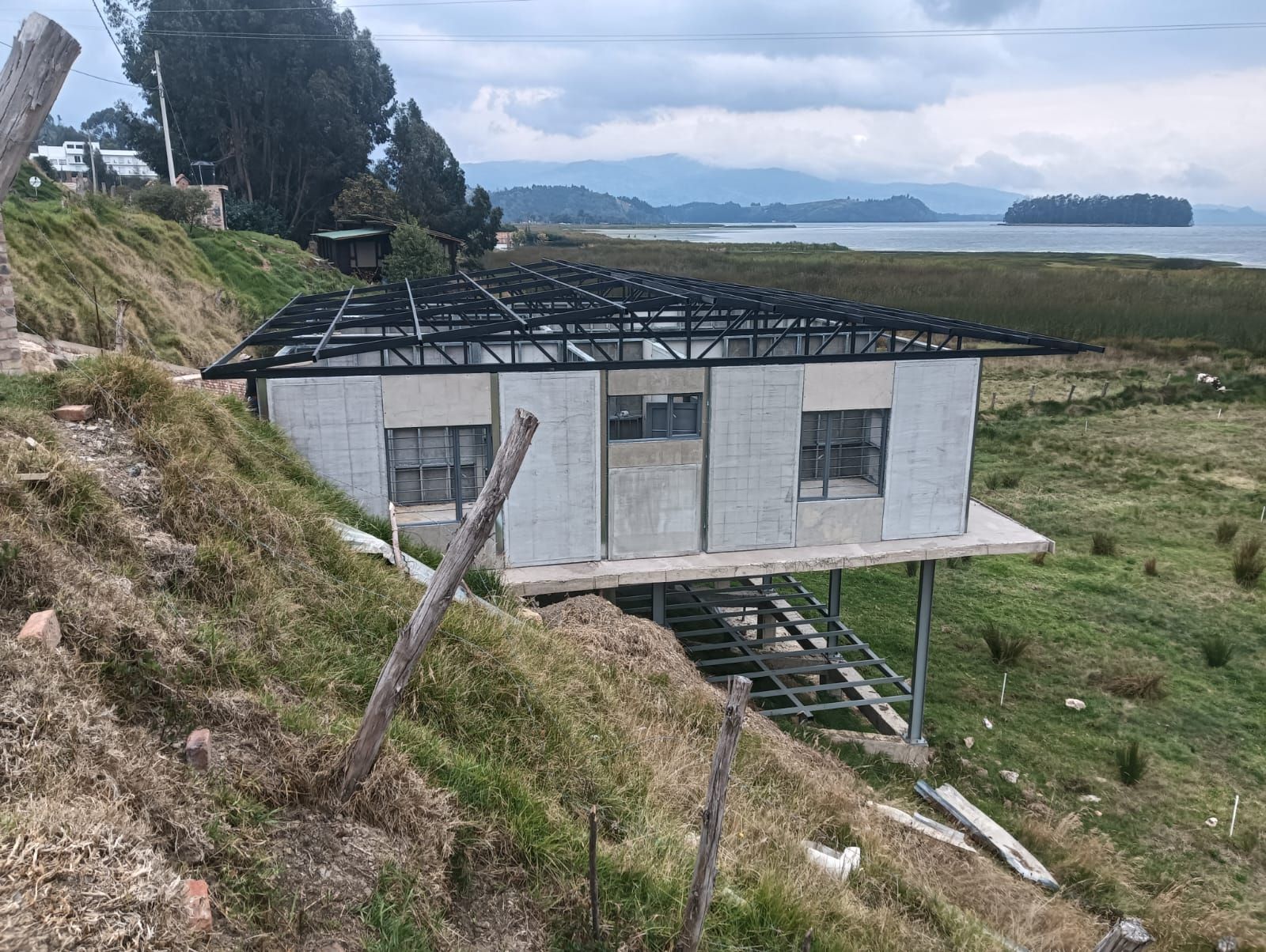 Pequeña casa blanca en una ladera cubierta de hierba con vistas al agua y a islas lejanas bajo un cielo nublado.