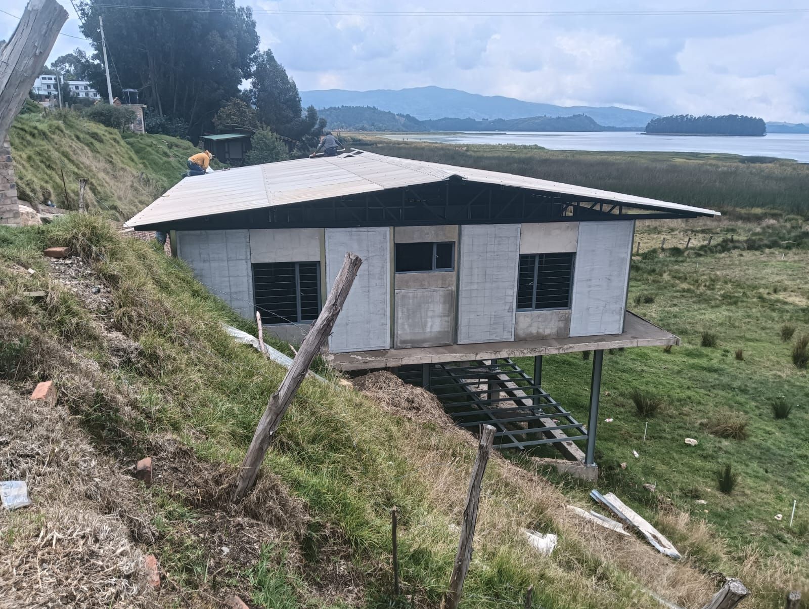 Pequeña casa blanca en la ladera de una colina, con techo negro, con vistas a un valle cubierto de hierba y a un agua lejana.