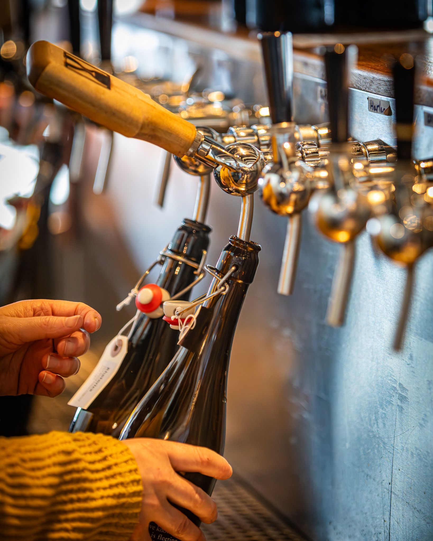 Hands filling brown bottles from a beer tap at a bar counter at Hill Farmstead Brewing's festival