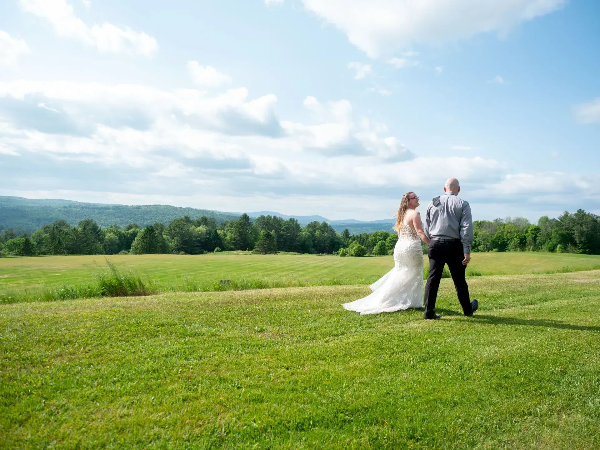 Bride and groom standing in a grassy field with a cloudy sky and distant trees