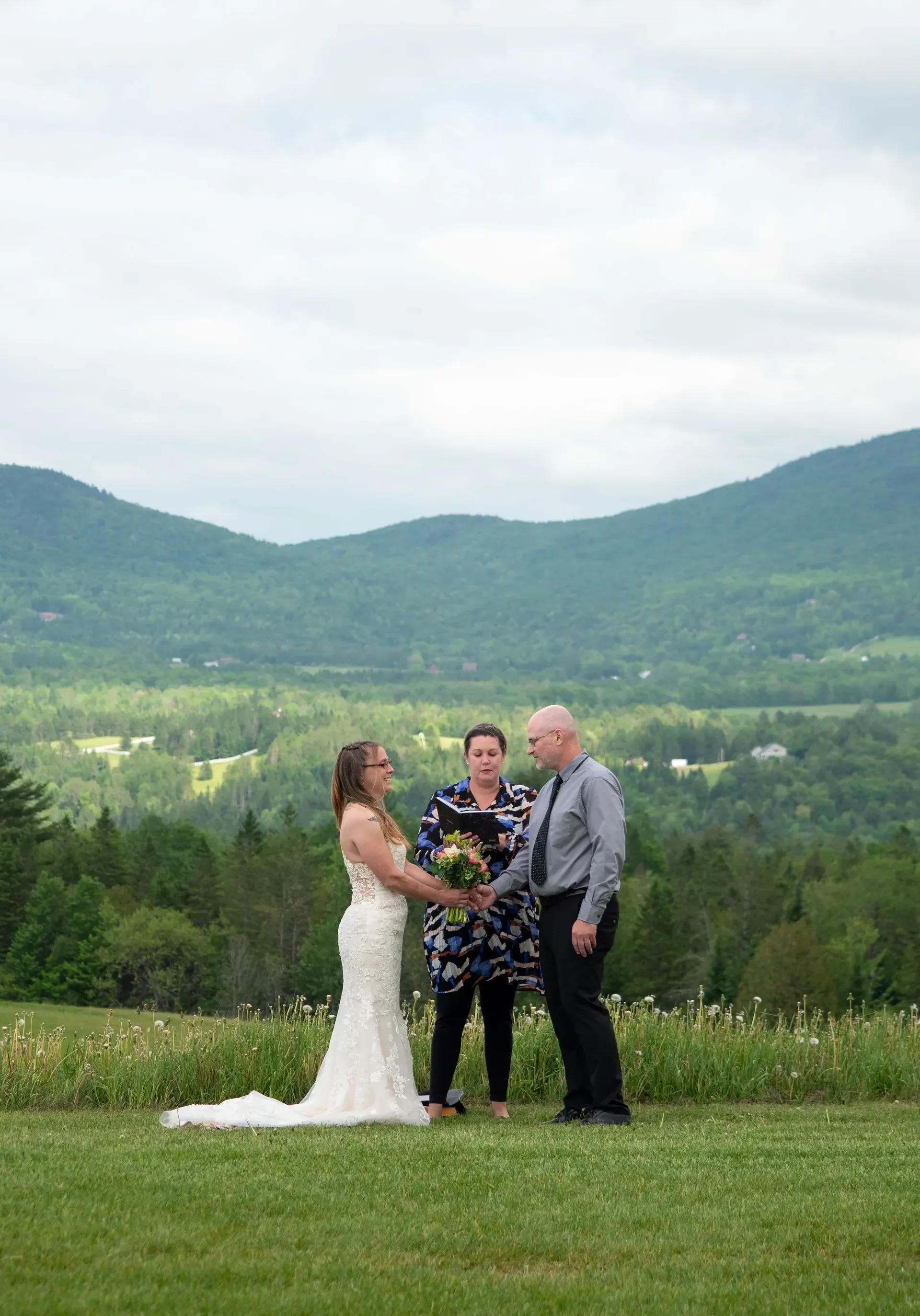 Bride and groom with officiant holding hands in a grassy mountain meadow