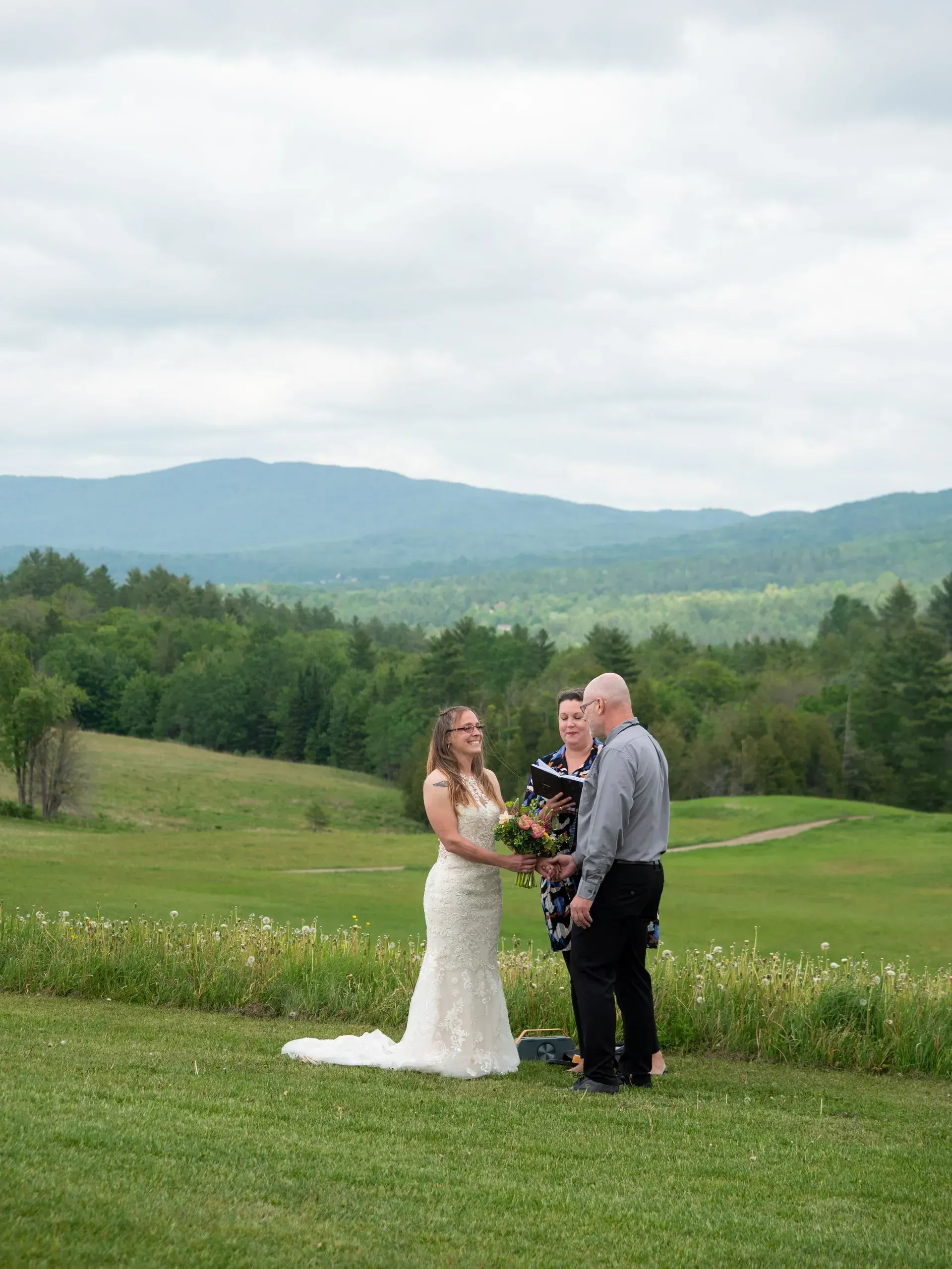 Wedding couple standing on a grassy hill with mountains in the background
