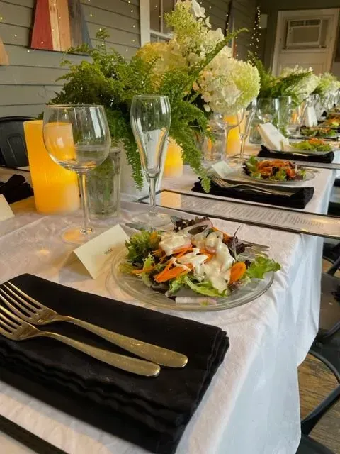 Elegant outdoor table setting with white flowers, candles, and plated salads on a black-and-white tablescape