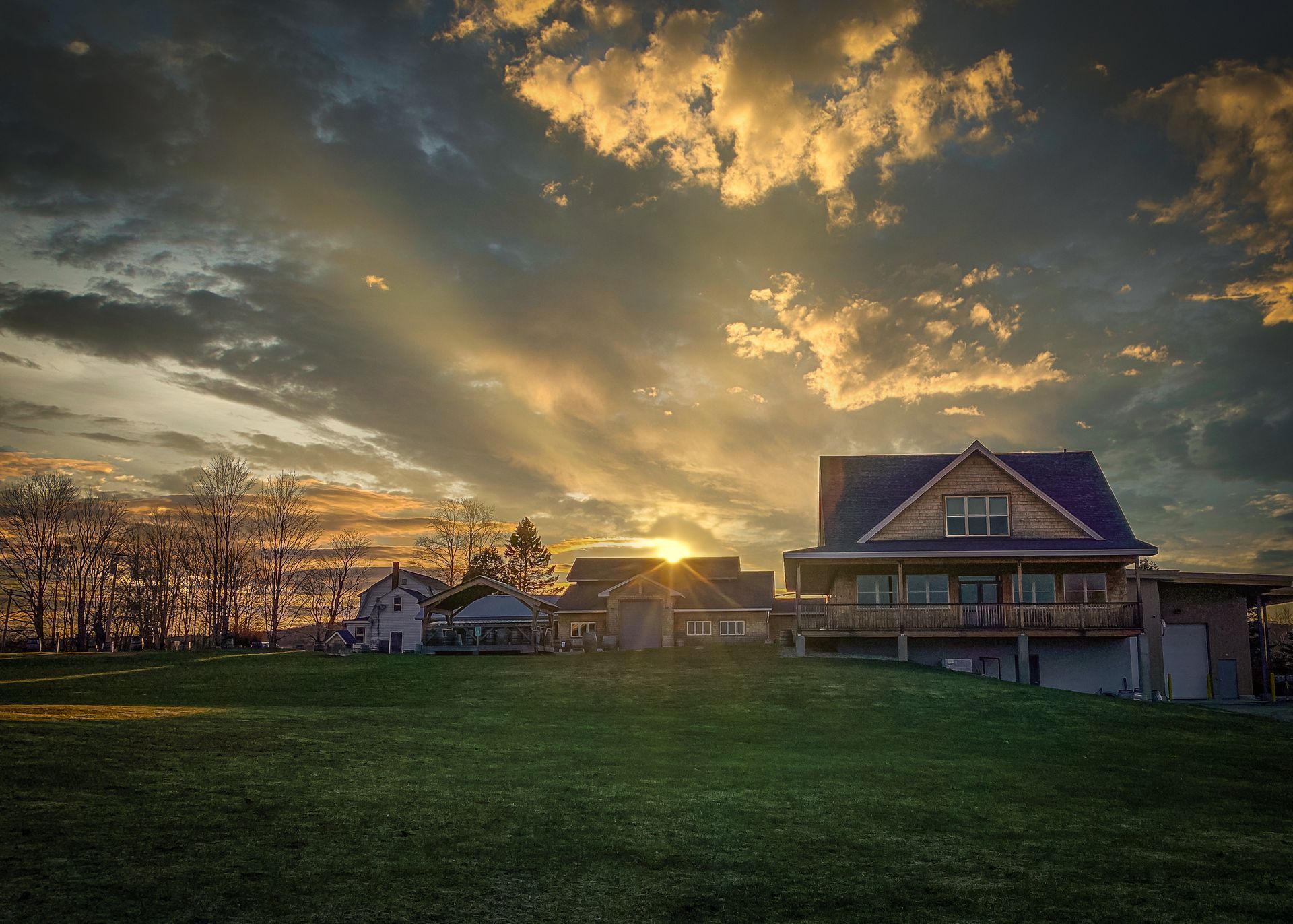 Sunset over Hill Farmstead Brewing's farmhouse and a grassy field beneath dramatic golden clouds