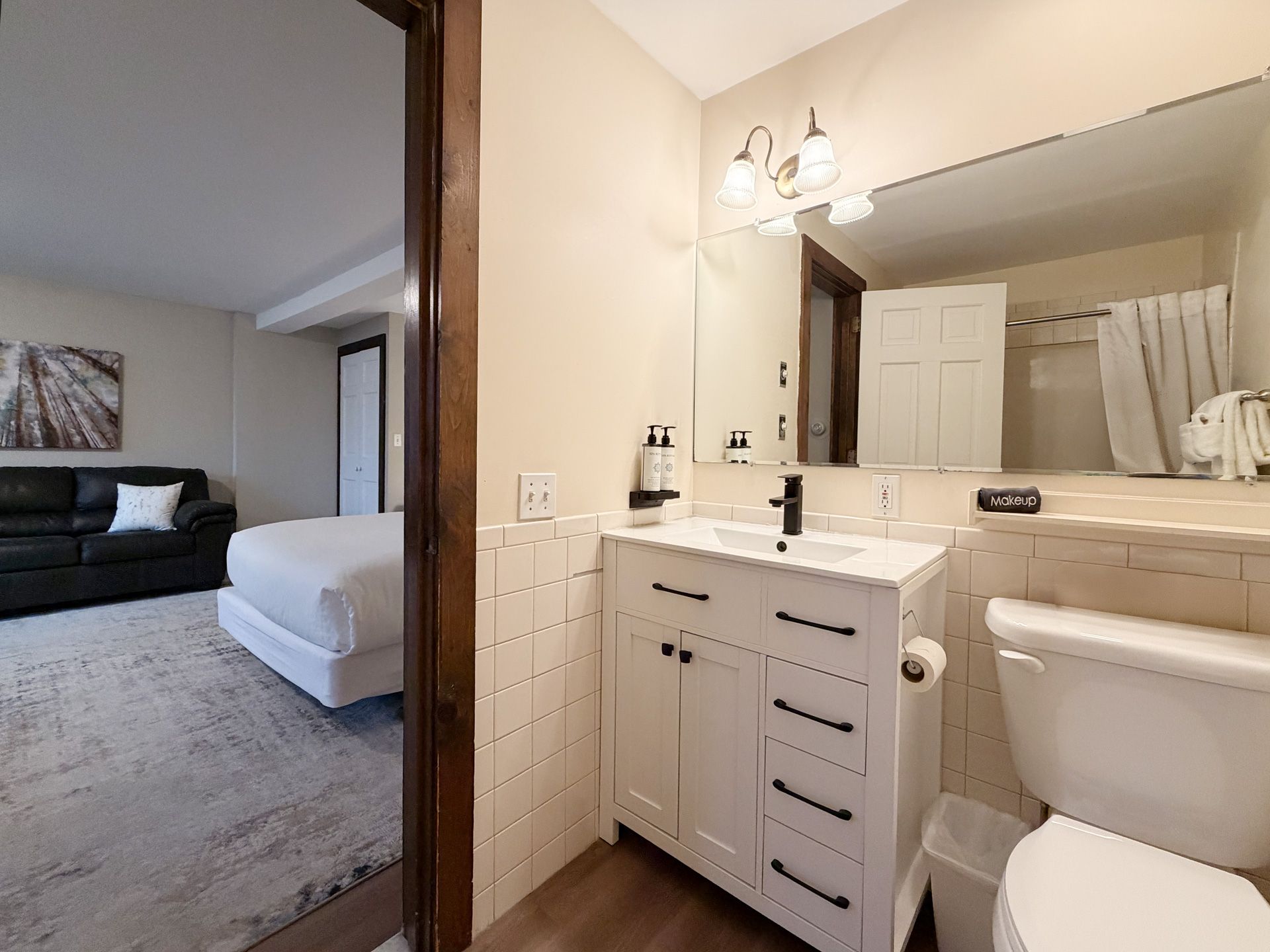 Bathroom vanity and toilet beside an open doorway to a bedroom with a bed and sofa.
