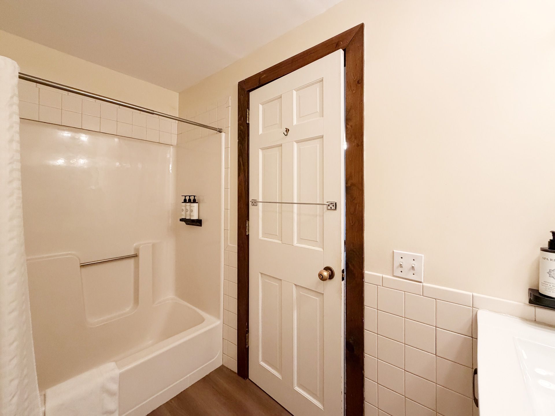 Bright bathroom with tub, white tile, and a closed paneled door beside a sink.