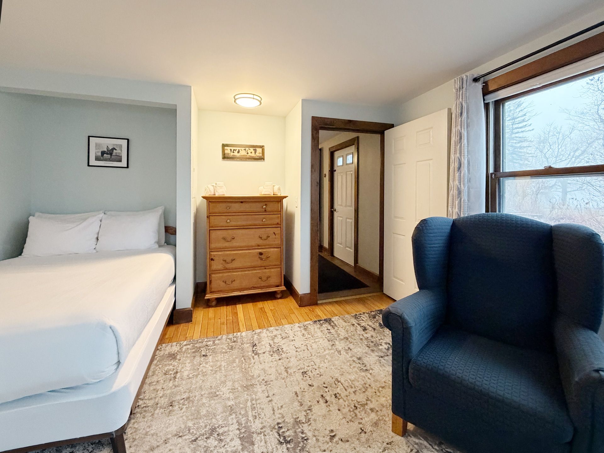 Cozy bedroom with twin bed, blue armchair, wooden dresser, and closet mirror under warm ceiling light