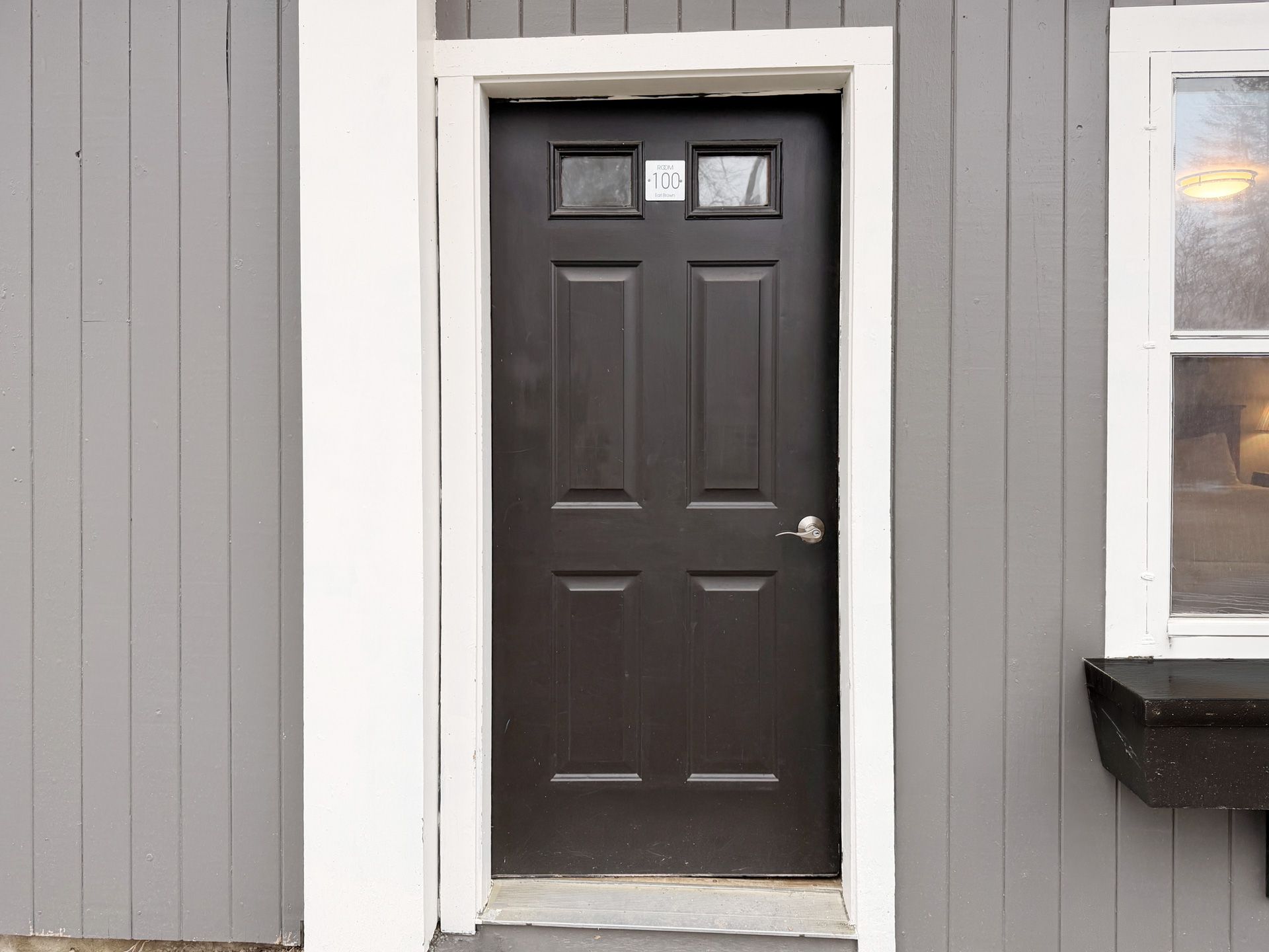 Dark brown front door with small windows in a gray building exterior