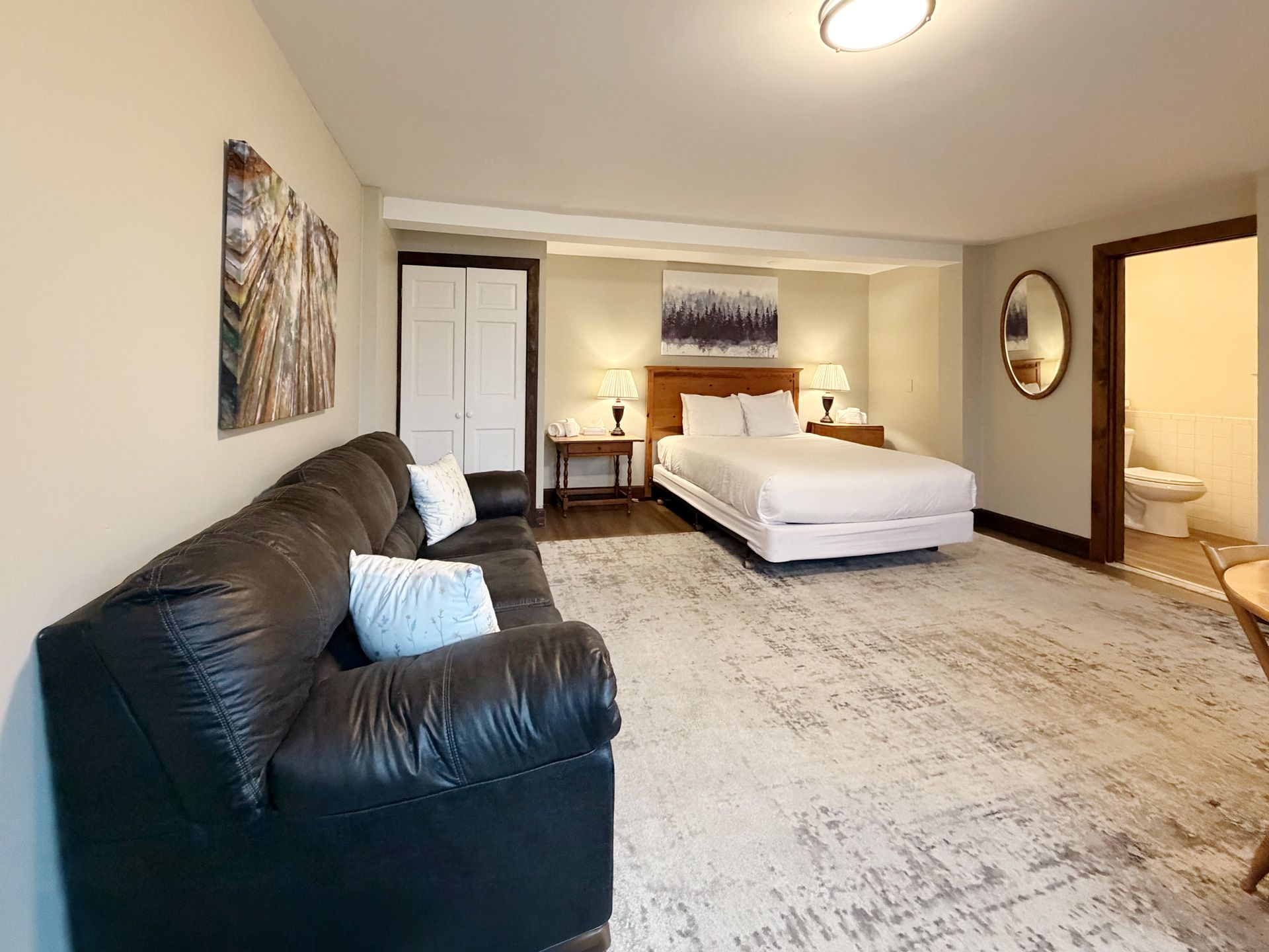 Spacious bedroom with a black sofa, white bed, carpeted floor, and warm lighting