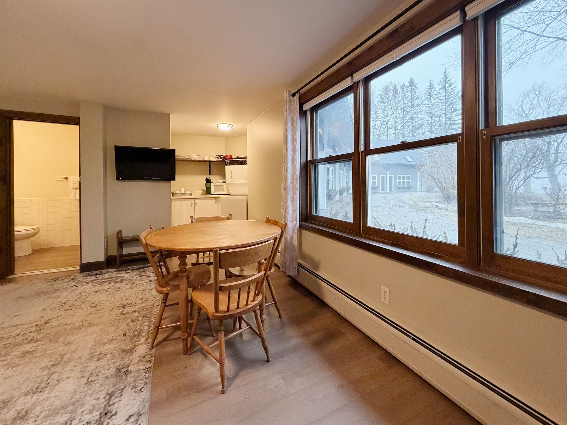 Dining area with wooden table and chairs beside large snowy windows in a warm apartment.