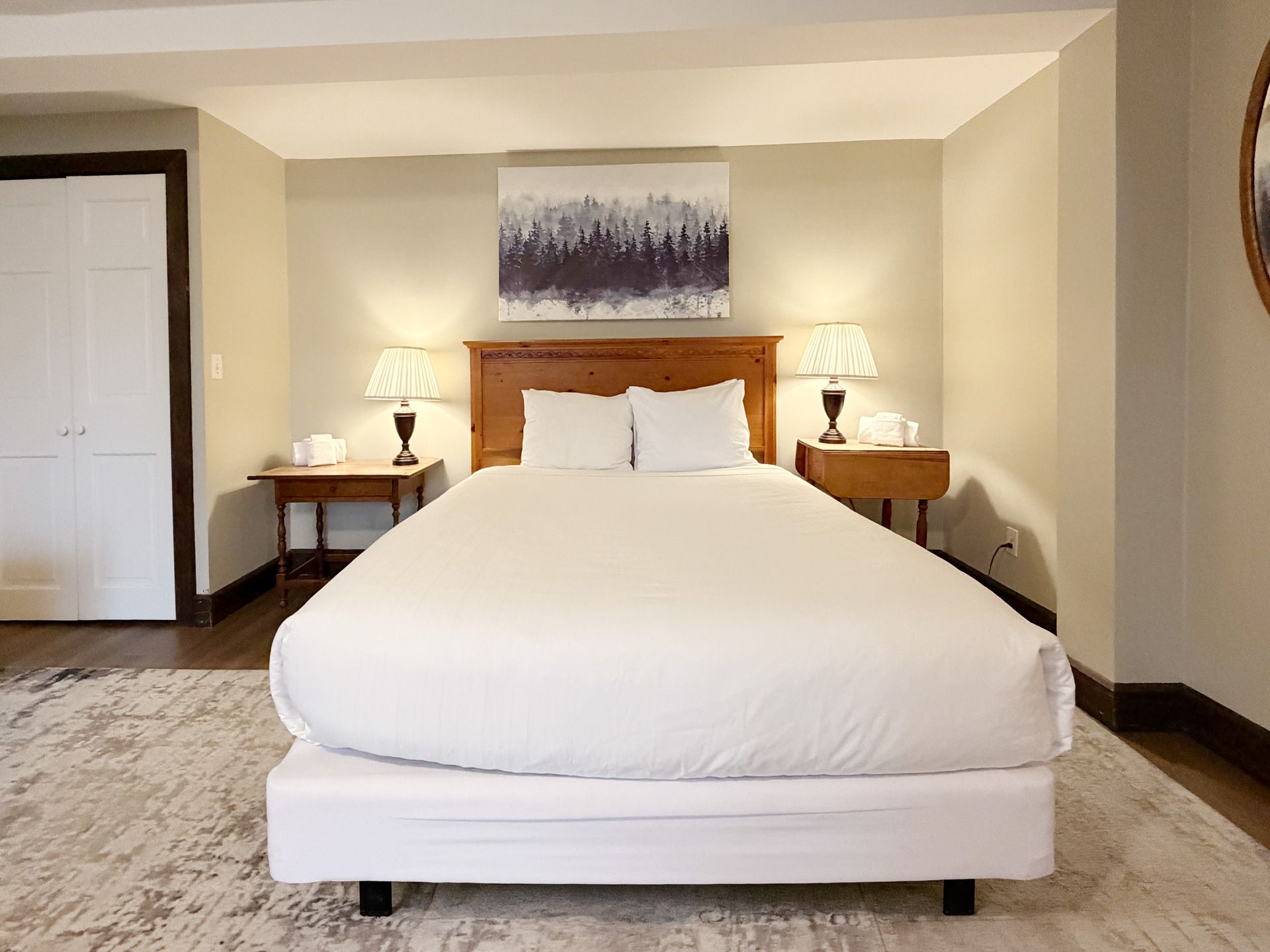 Neatly made bed in a beige bedroom with bedside lamps and wall art