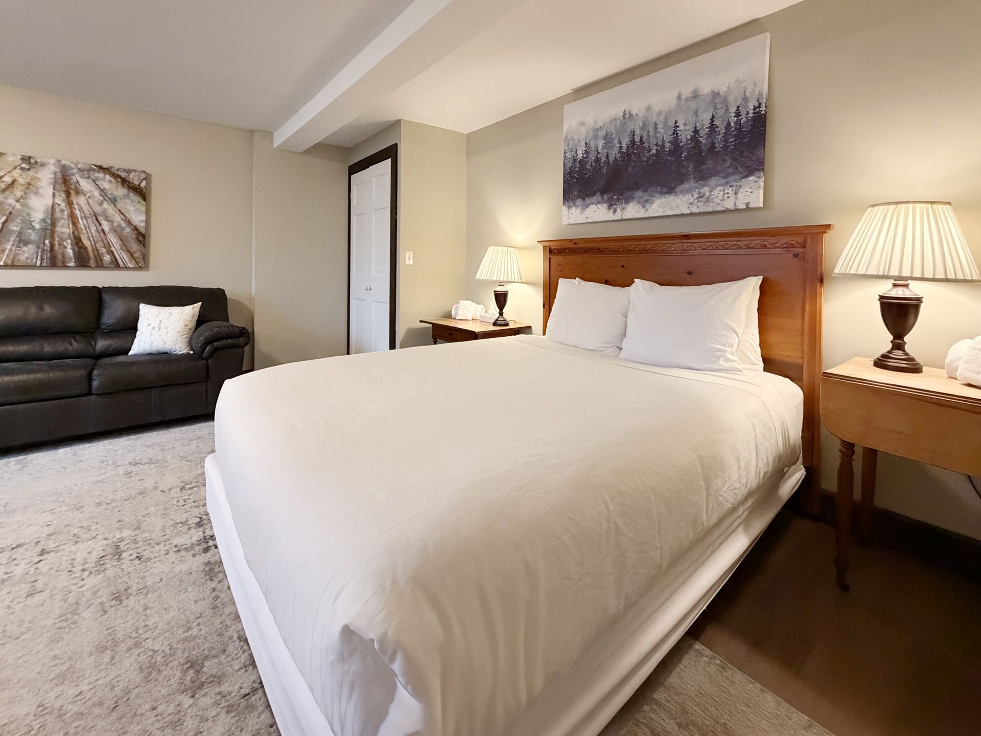 Cozy bedroom with a queen bed, bedside lamps, sofa, and wall art in neutral tones