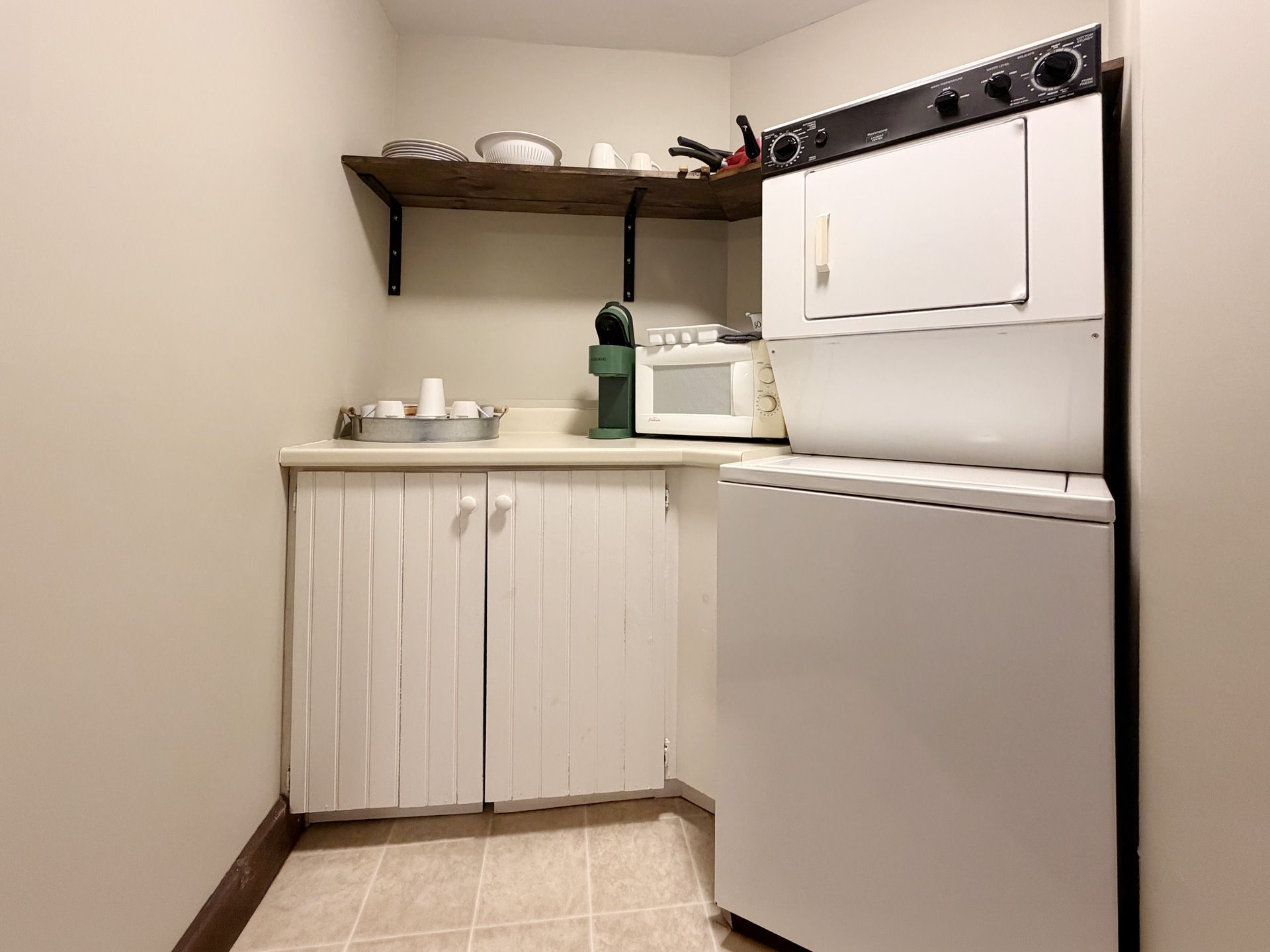 Small kitchen corner with white cabinets, sink, open shelf, and white stove and refrigerator.