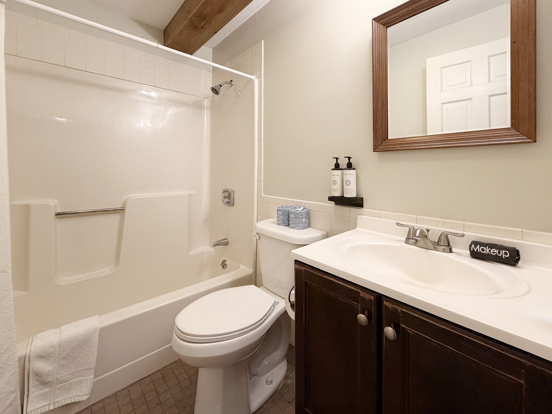 Small bathroom with tub-shower, toilet, and dark wood vanity with sink and mirror