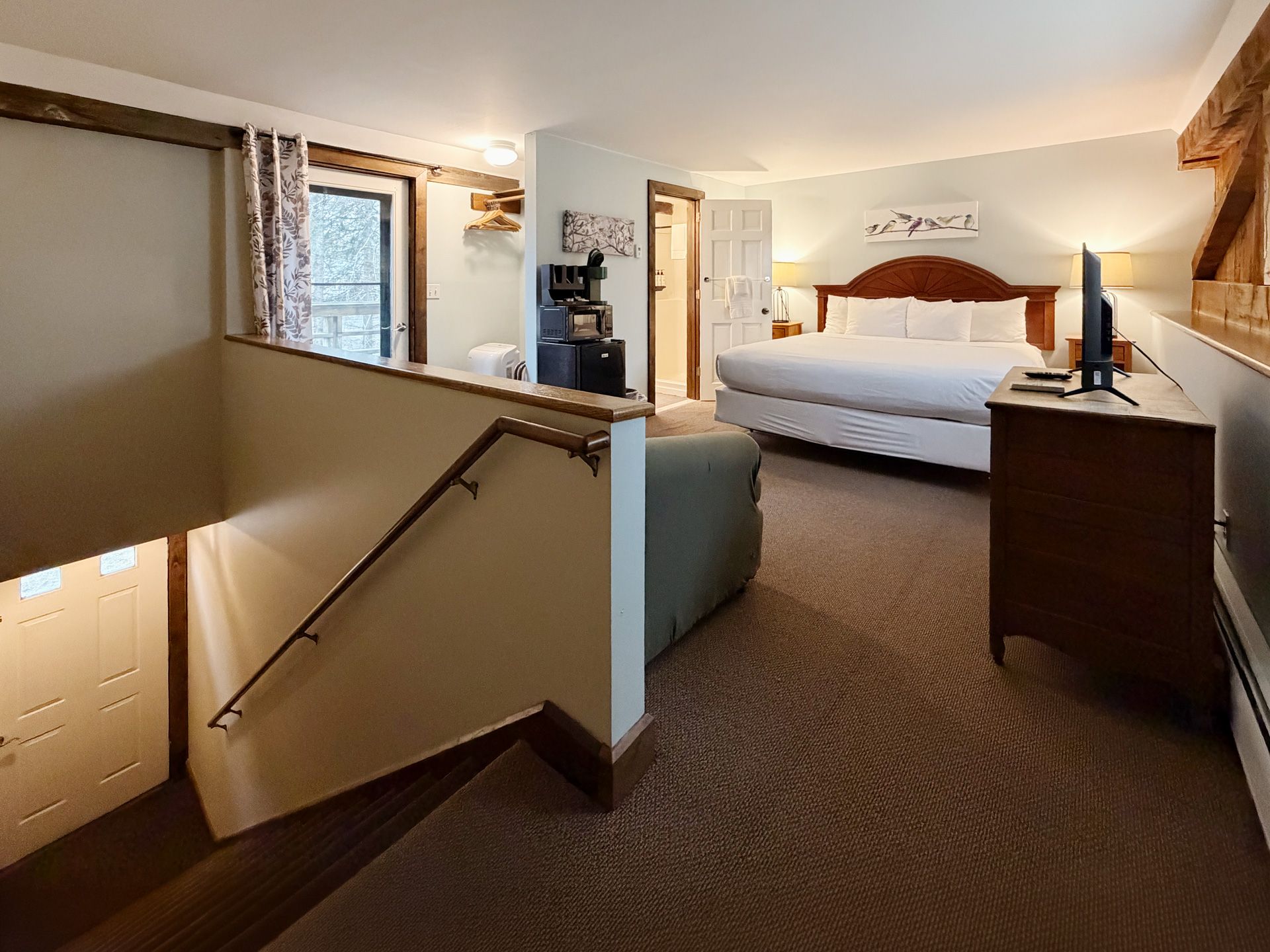 Hotel bedroom with a king bed, nightstands, and a stair railing in the foreground