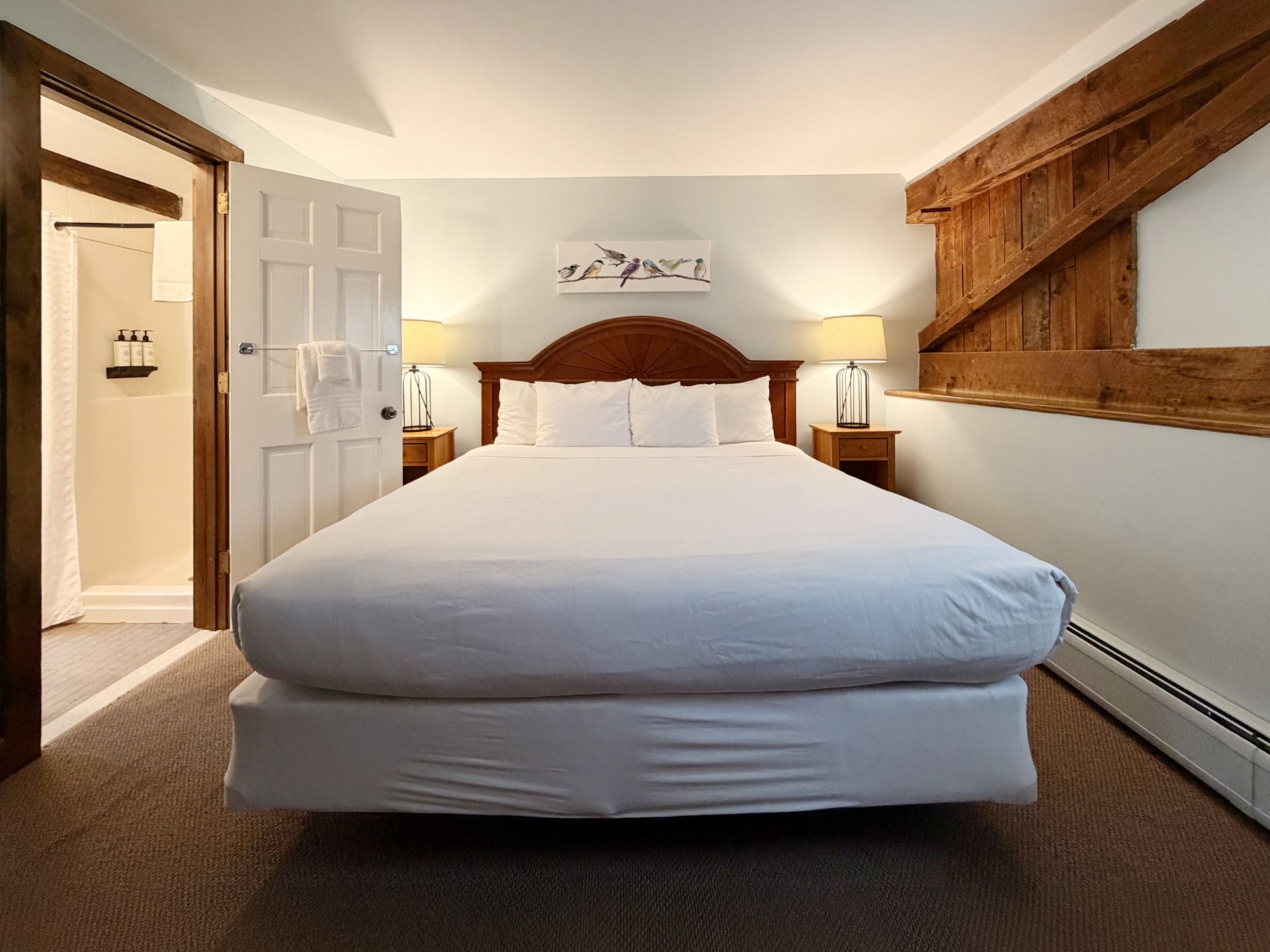 Neatly made hotel bedroom with a large bed, bedside lamps, and rustic wood wall accents.