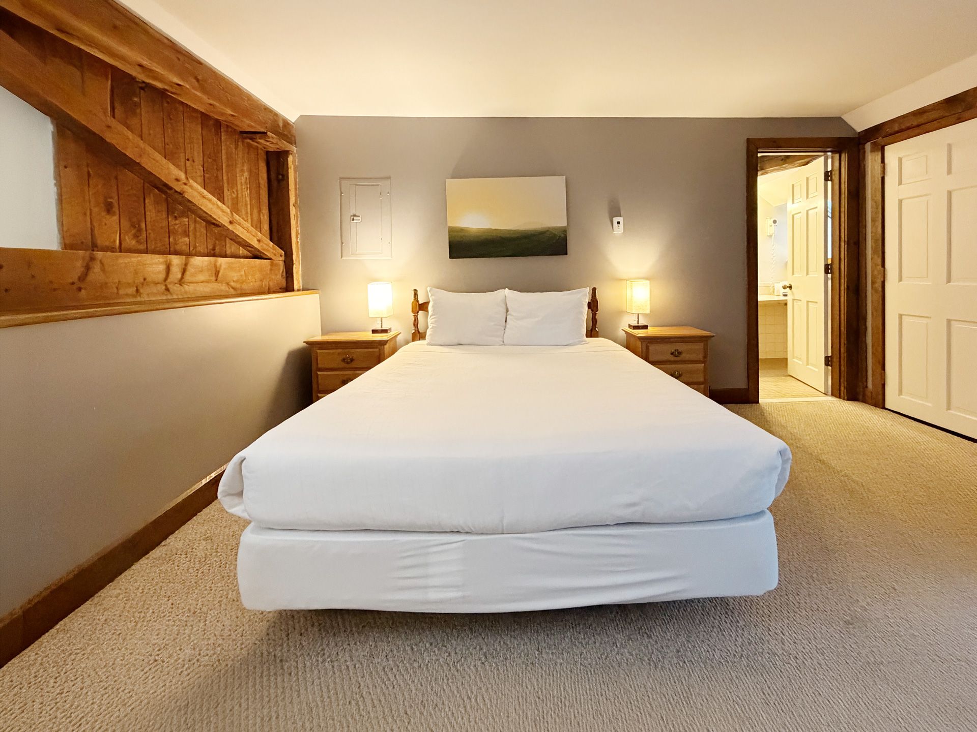 Bright bedroom with a white bed, bedside lamps, and open doorway to a bathroom