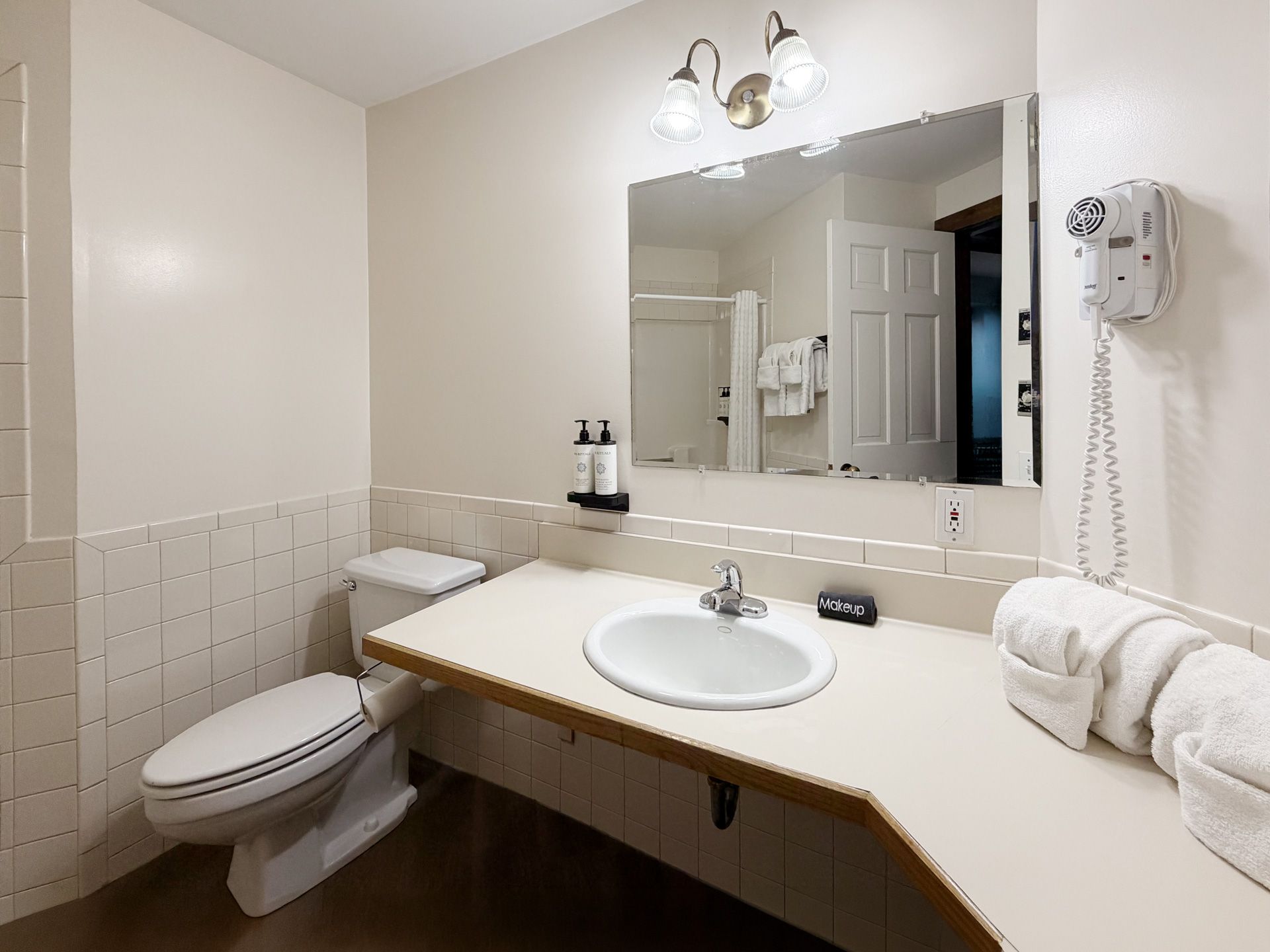 Accessible bathroom with vanity, mirror, toilet, sink, towels, and wall-mounted phone.