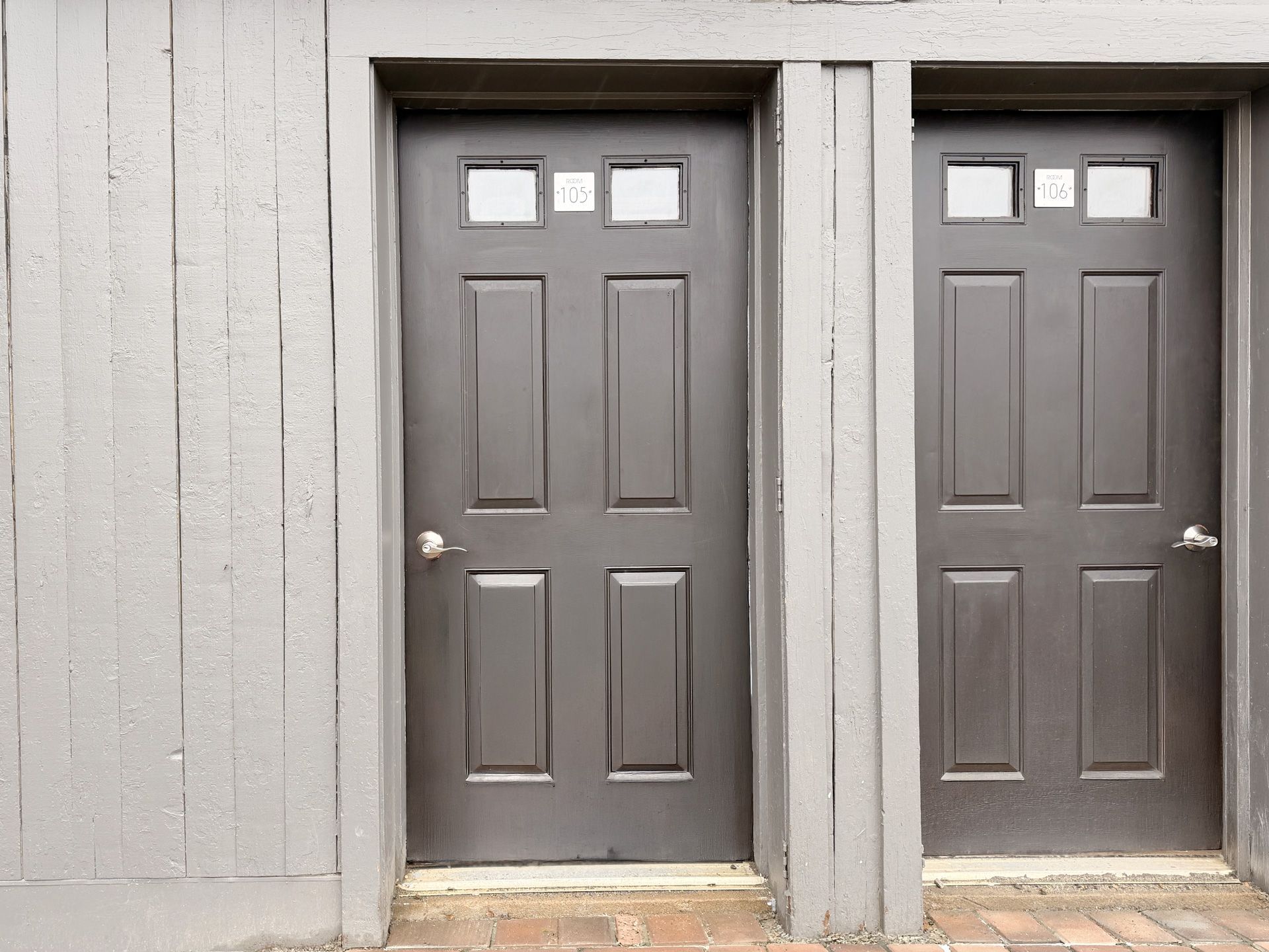Two gray doors in a light gray exterior wall, each with small windows near the top.