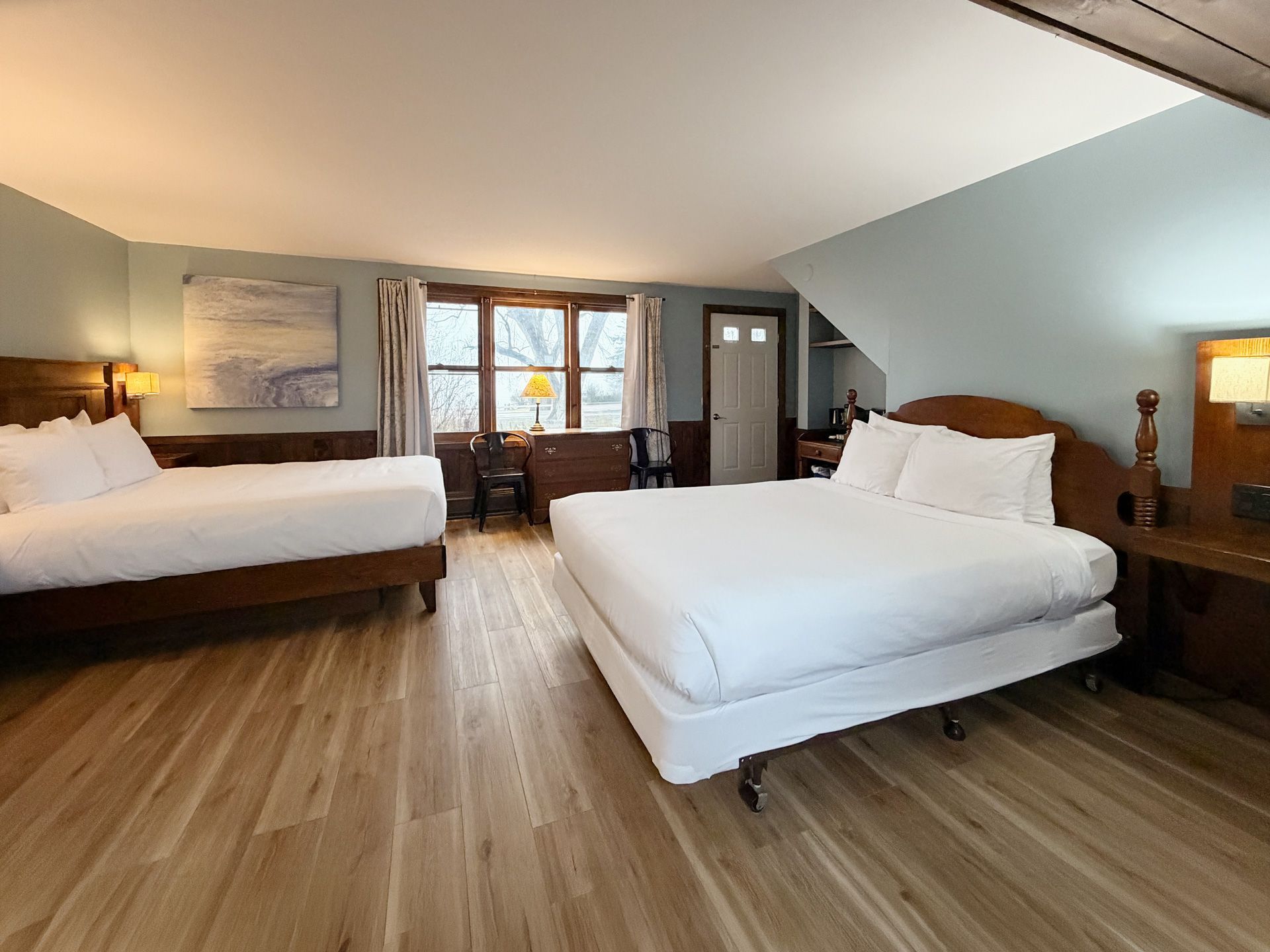 Spacious bedroom with two white beds, wood floors, and a window seat in warm light